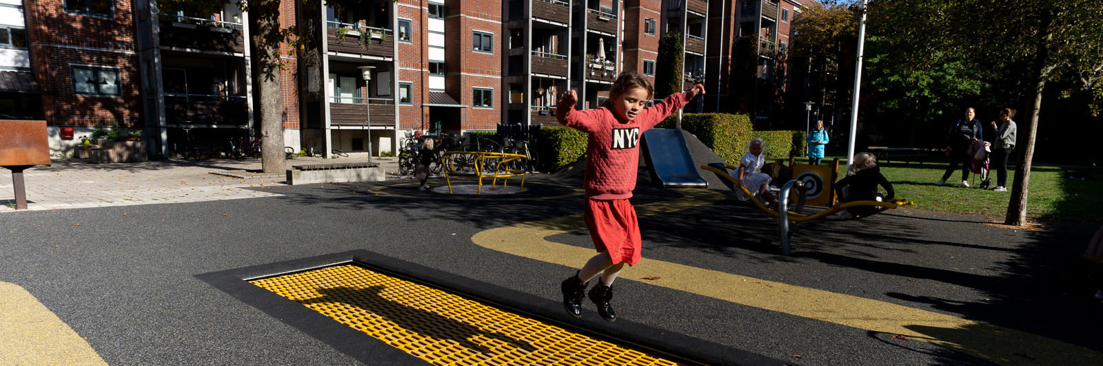 A child is jumping in the air from an in ground trampoline at a playground.